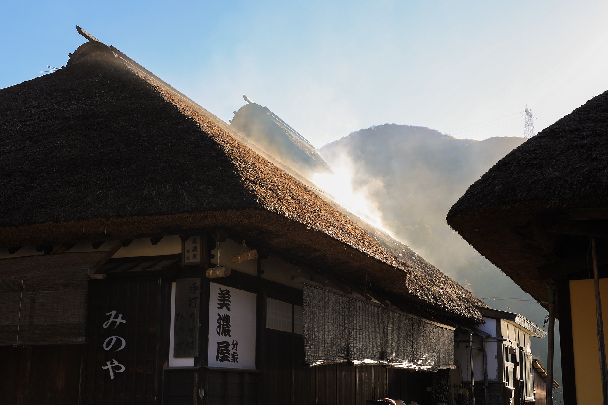 大内宿の茅葺き屋根に朝日が差し込み、屋根から湯気のような白い水蒸気が立ち上る秋の朝の風景